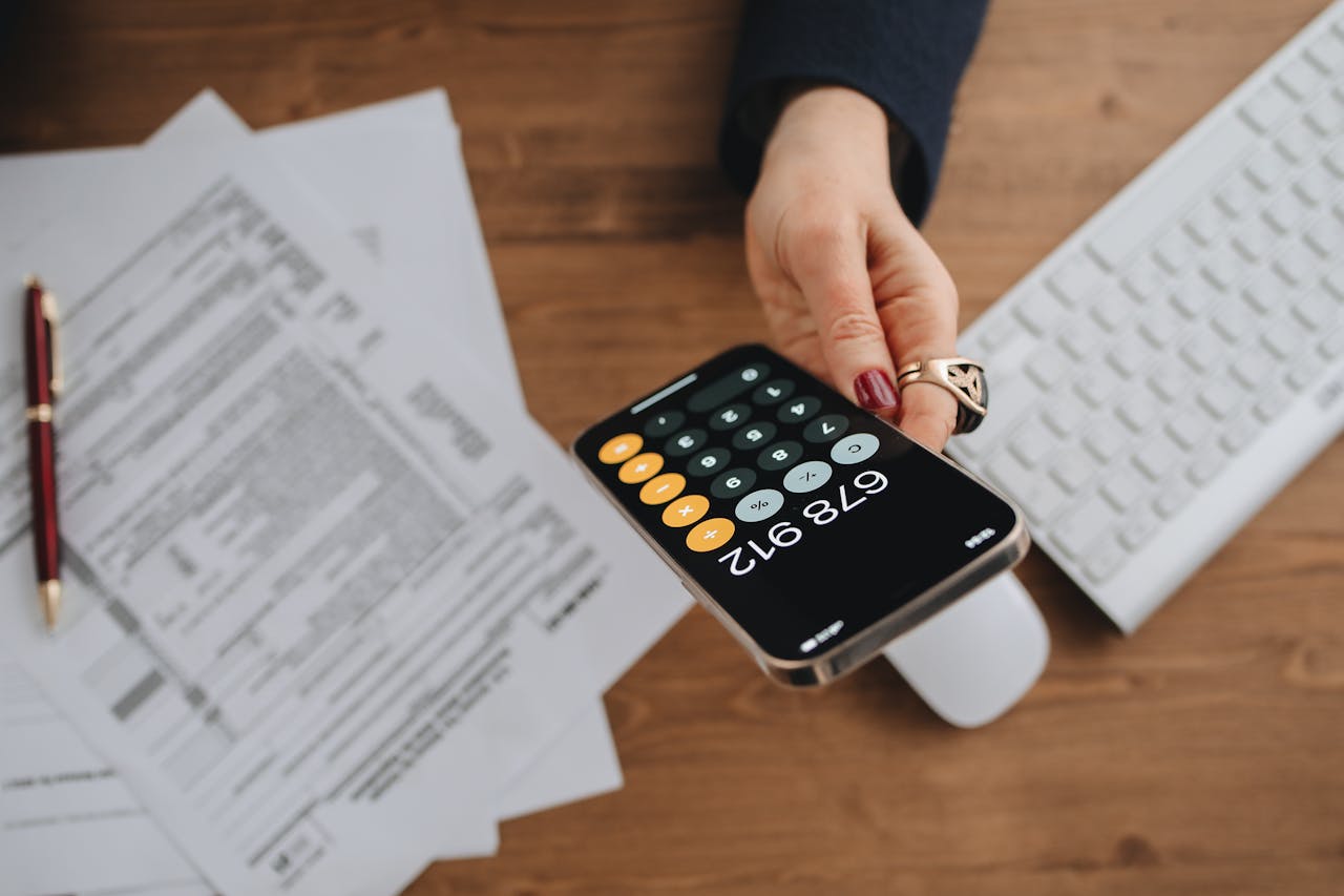 Calculator displayed on a smartphone held by a person, with legal documents and a pen on a wooden desk.