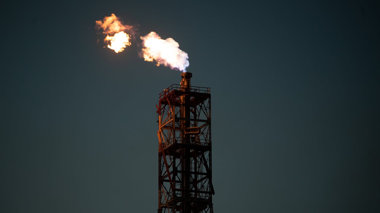 Flare igniting at the top of an industrial smokestack against a dark sky.