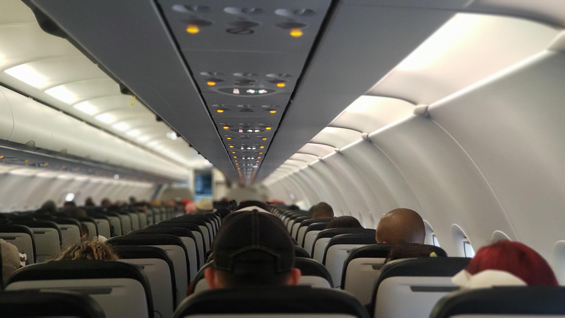Interior of an airplane with rows of seats and passengers seated, showing a well-lit cabin environment.