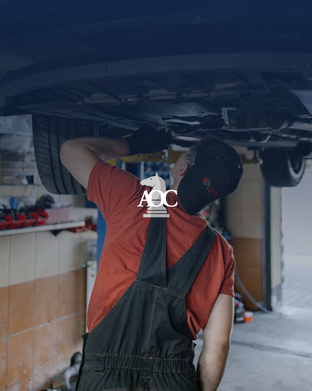 Mechanic inspecting vehicle undercarriage in auto repair shop.