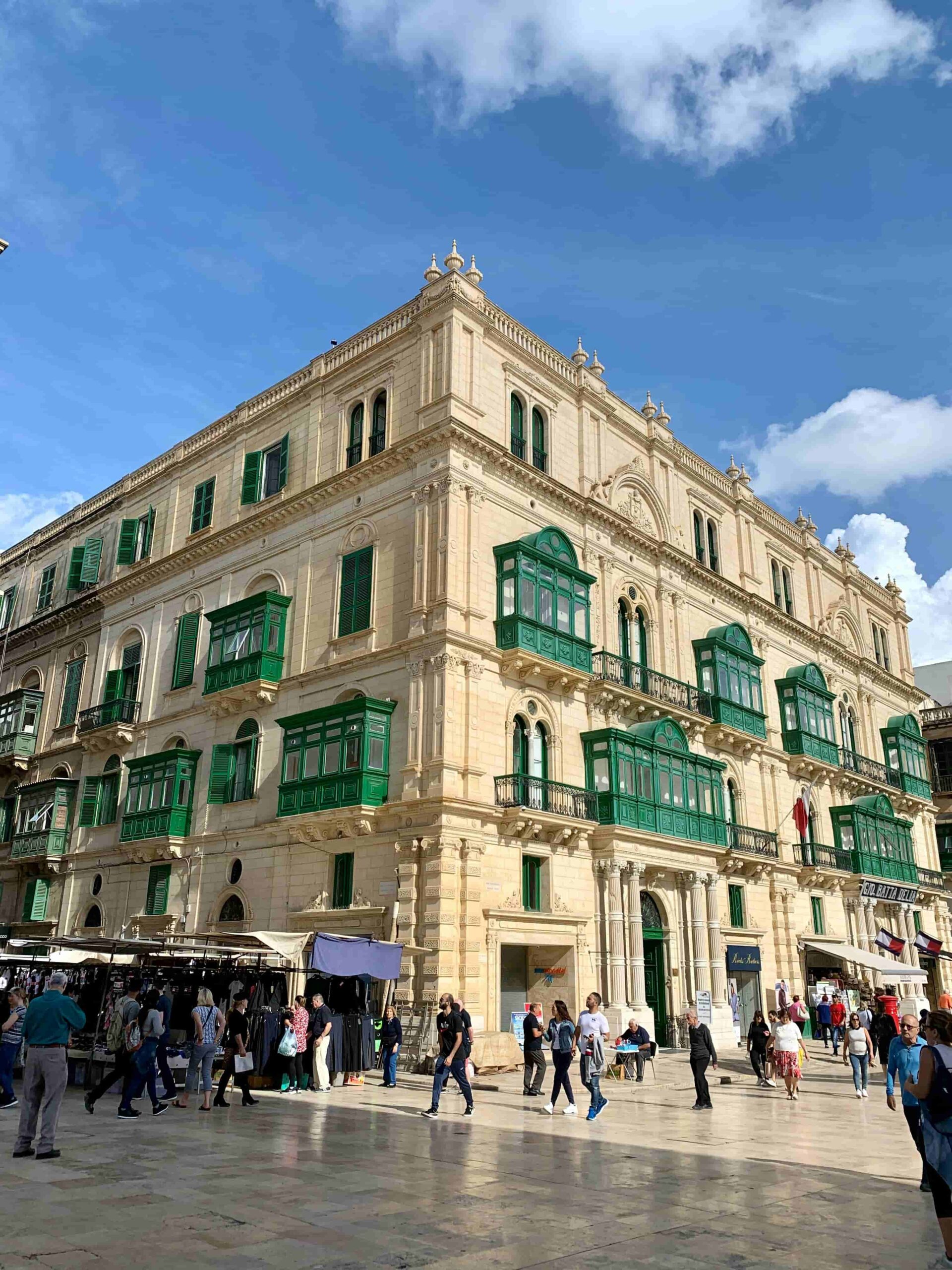 Historic building with green shutters, surrounded by pedestrians in a bustling square.