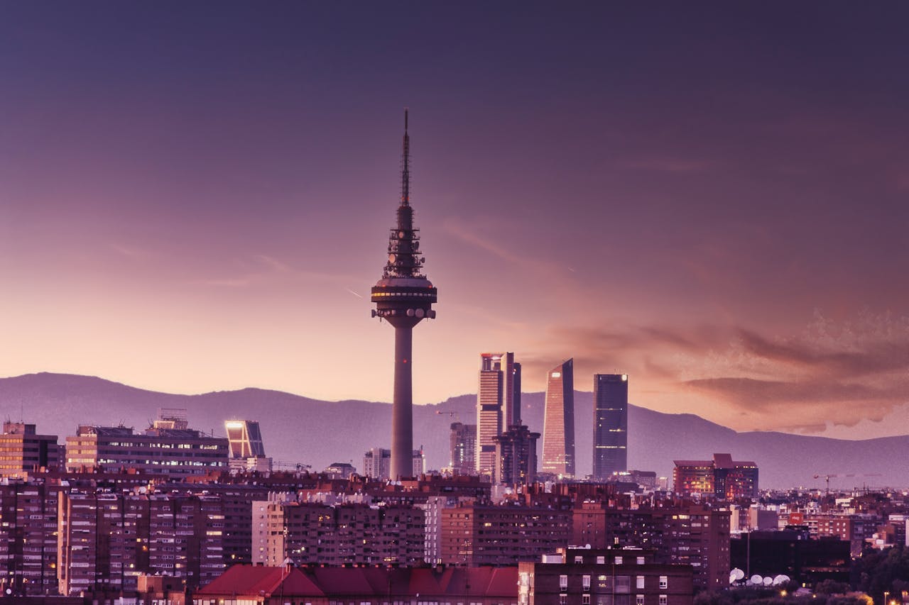 City skyline at sunset featuring modern skyscrapers and a prominent communication tower.