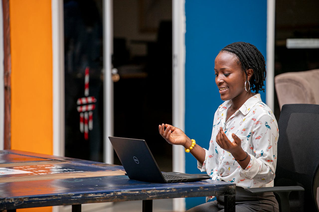 Professional discussing ideas while seated at a table with a laptop in a casual office setting.