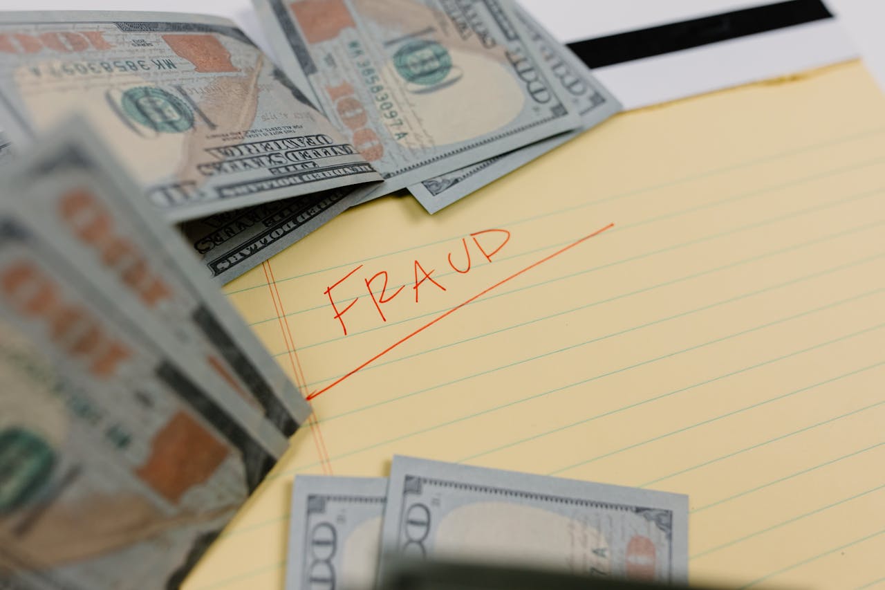 Yellow legal pad with the word "FRAUD" written in red next to scattered hundred-dollar bills.