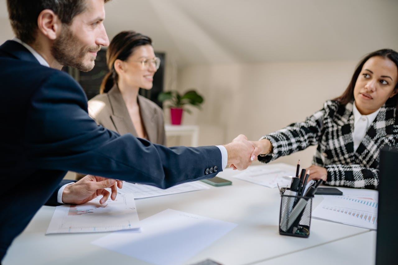 Attorney shaking hands with a client at a desk, discussing legal documentation in a modern office setting.
