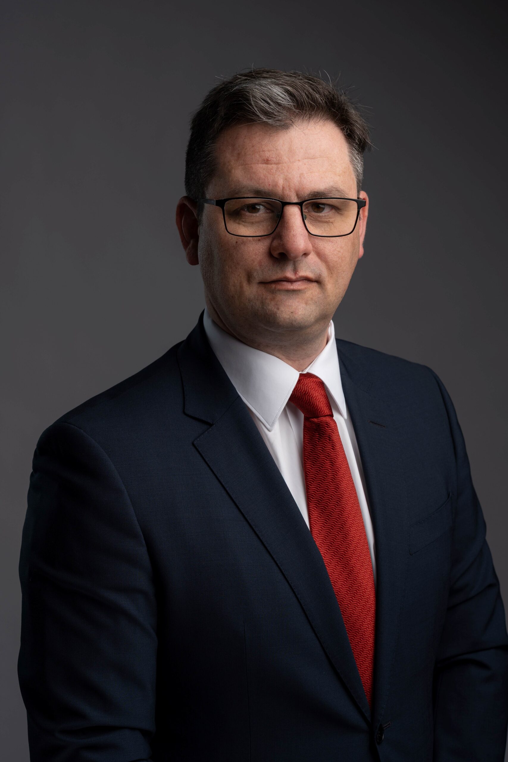 Lawyer in a dark suit and red tie, looking confidently at the camera against a neutral background.