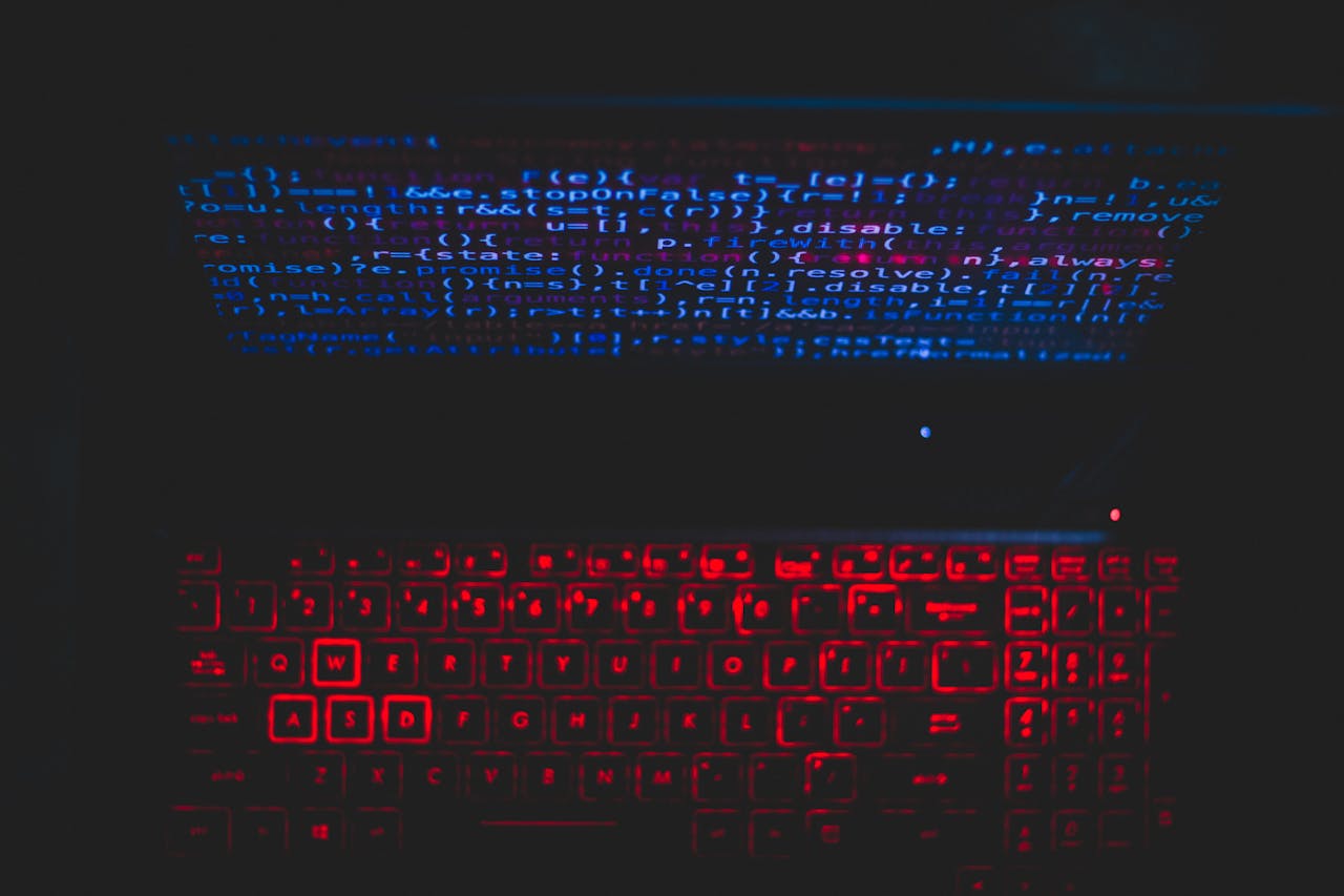 Computer keyboard with illuminated keys and programming code displayed on the screen.