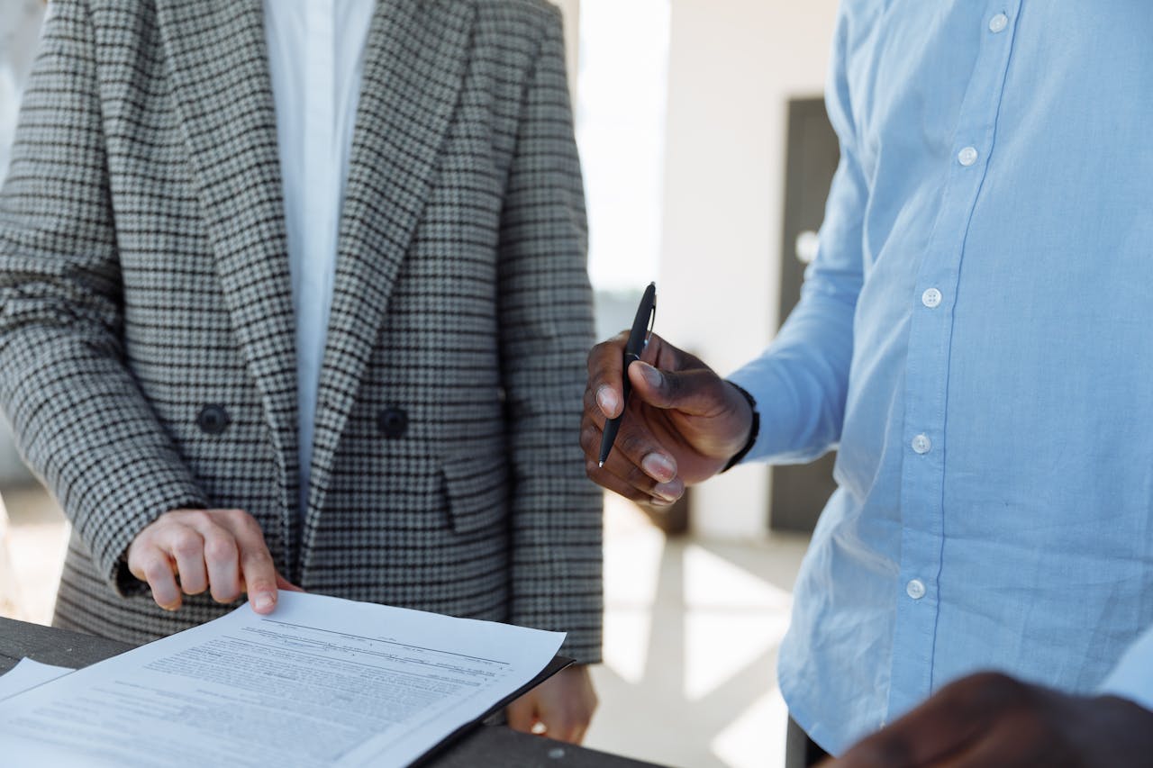 Two individuals discussing legal documents at a table, one pointing and the other holding a pen.