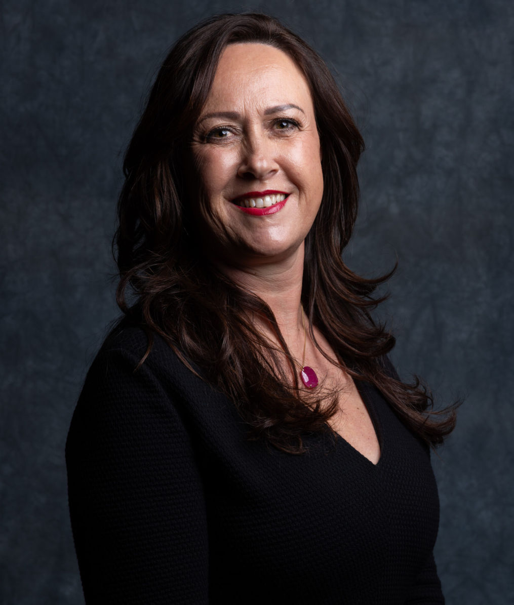Professional woman with long hair smiling against a textured background, wearing a black top and necklace.