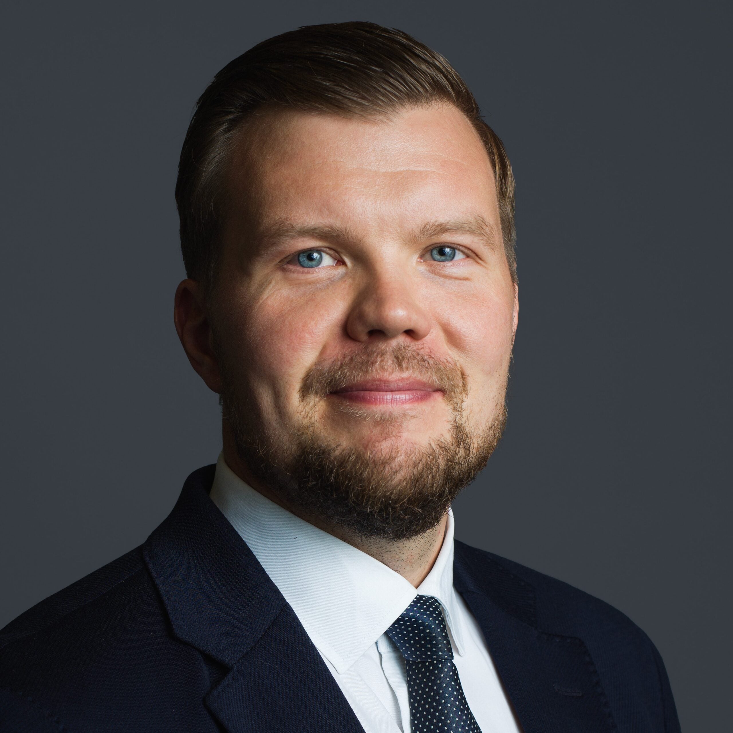 Attorney in a suit with a beard and blue eyes, facing the camera against a neutral gray background.