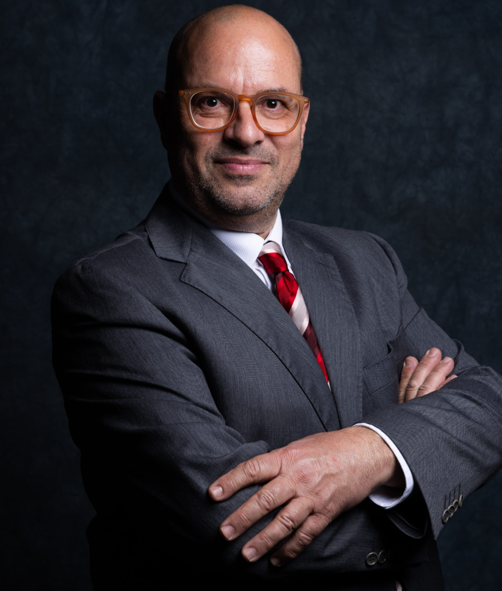 Attorney posing confidently with arms crossed, wearing a suit and tie against a dark textured background.
