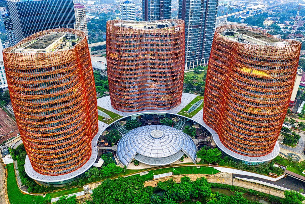 Modern office complex featuring three tall, orange-framed towers and a circular glass atrium surrounded by greenery.