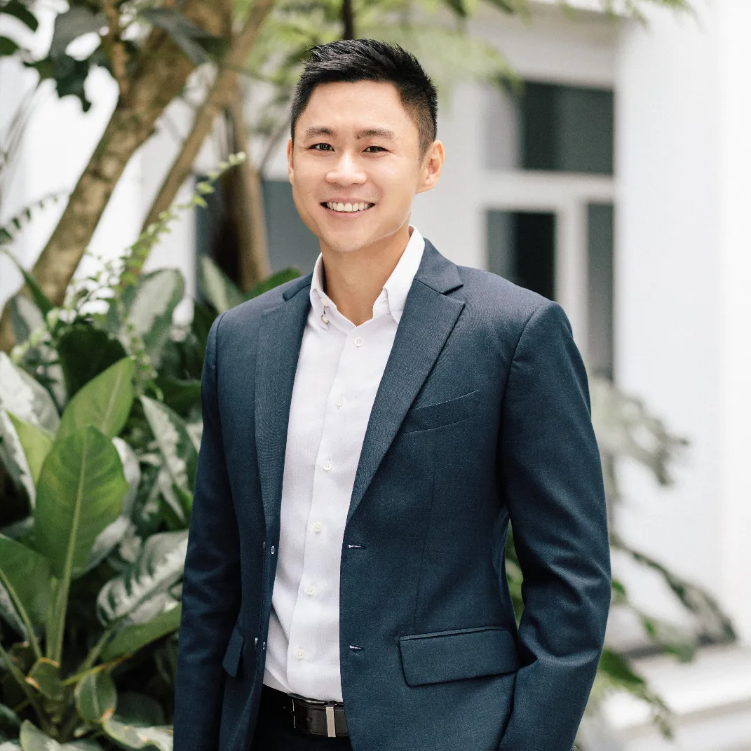 Smiling professional in a suit standing among indoor plants in a modern office setting.