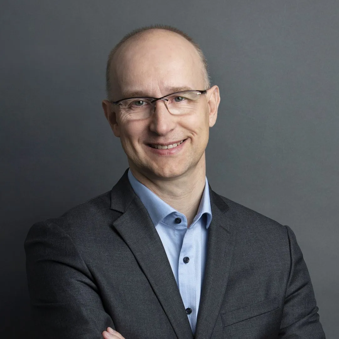 Legal professional smiling while standing with arms crossed against a neutral background.