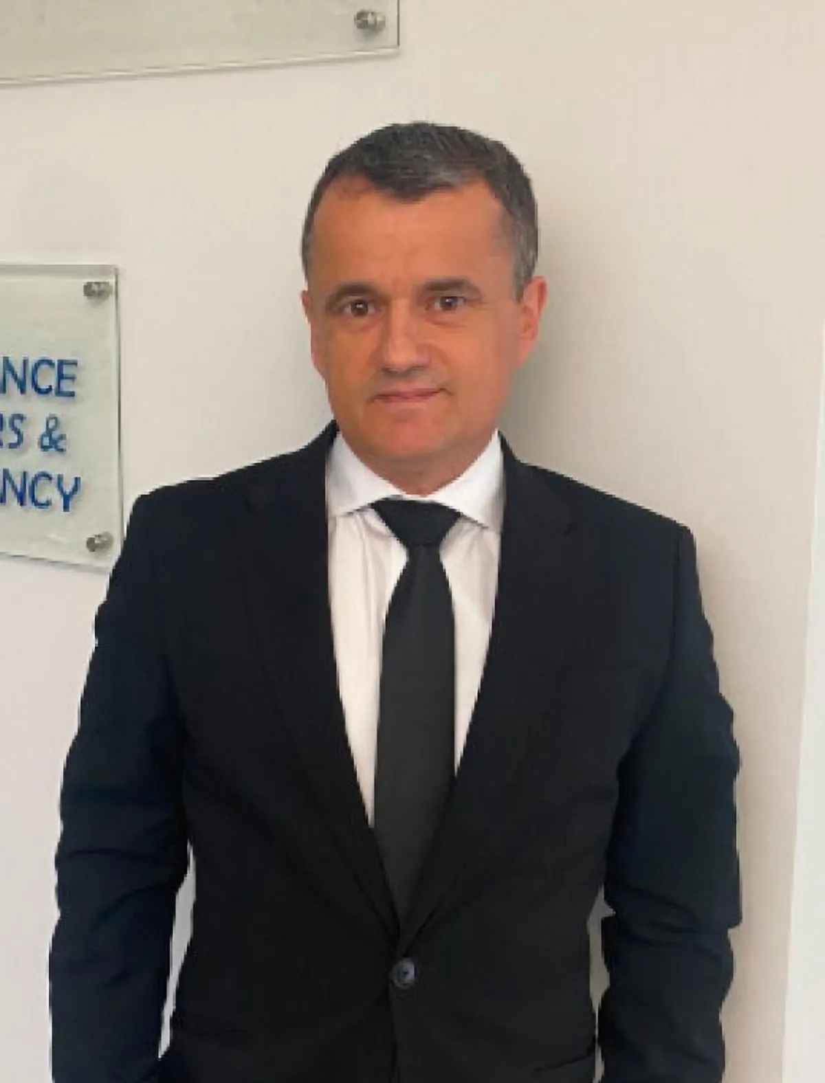 Lawyer in formal attire standing in front of office signage related to legal services and consultancy.
