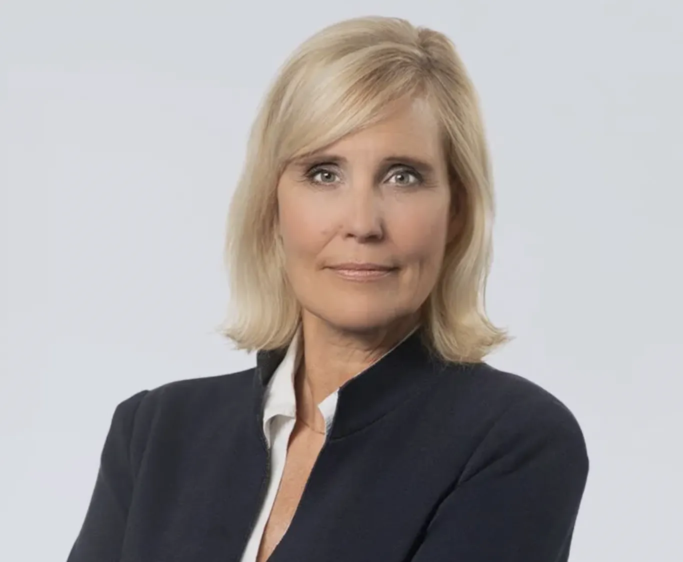Professional woman in a blazer posing confidently with arms crossed against a neutral background.