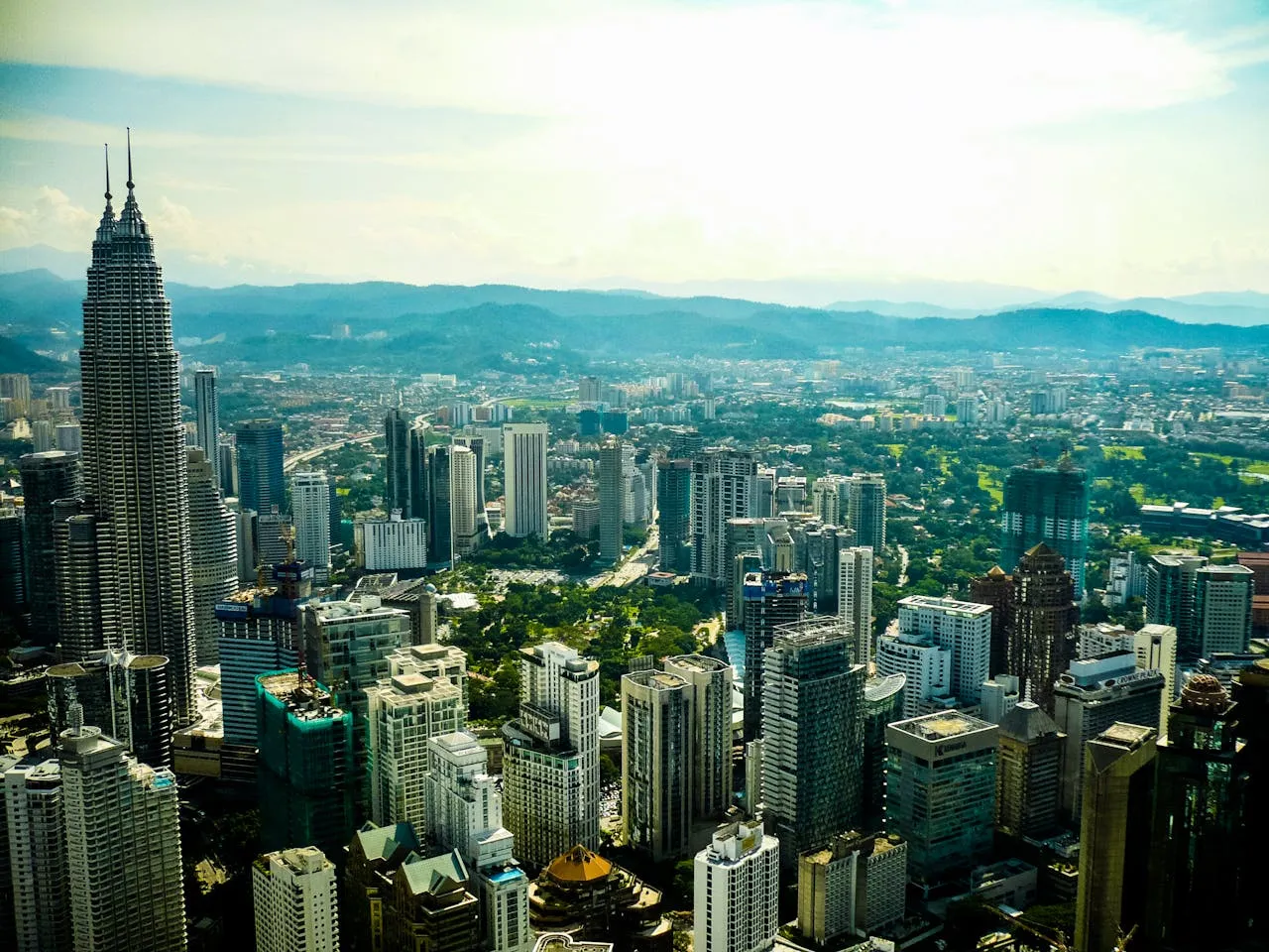 Cityscape view featuring tall modern skyscrapers and green spaces with hills in the background.