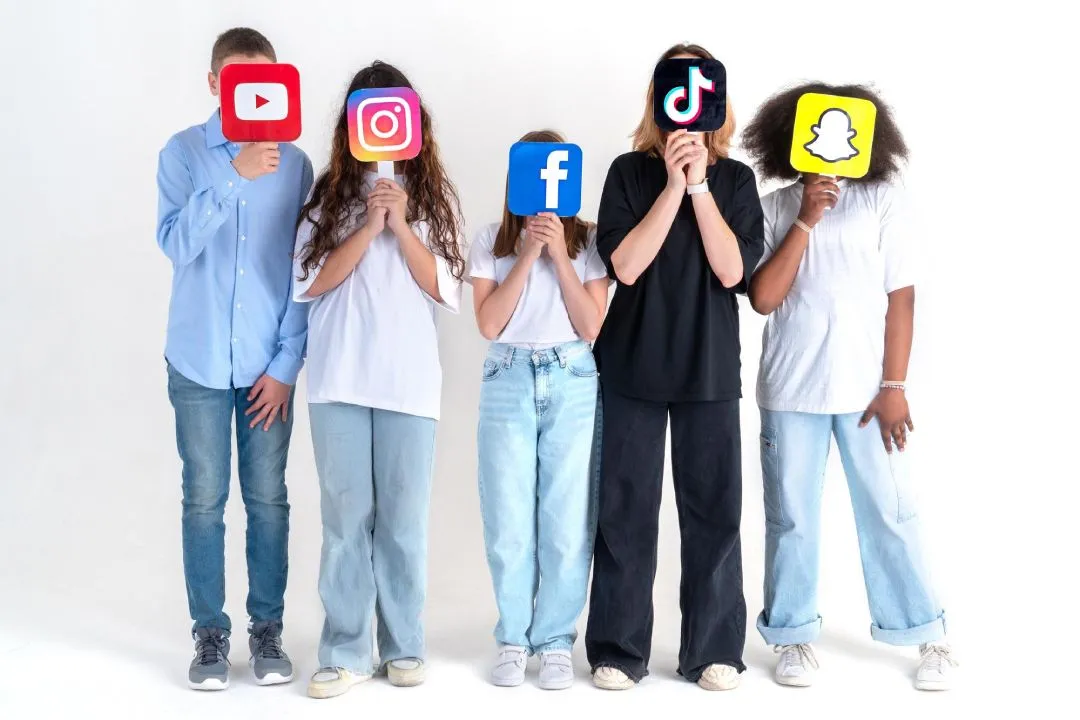 Group of five individuals holding social media logo signs in front of their faces, posing against a white background.