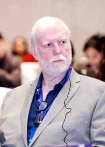 Senior professional listening attentively during a conference with a notepad in a neutral setting.