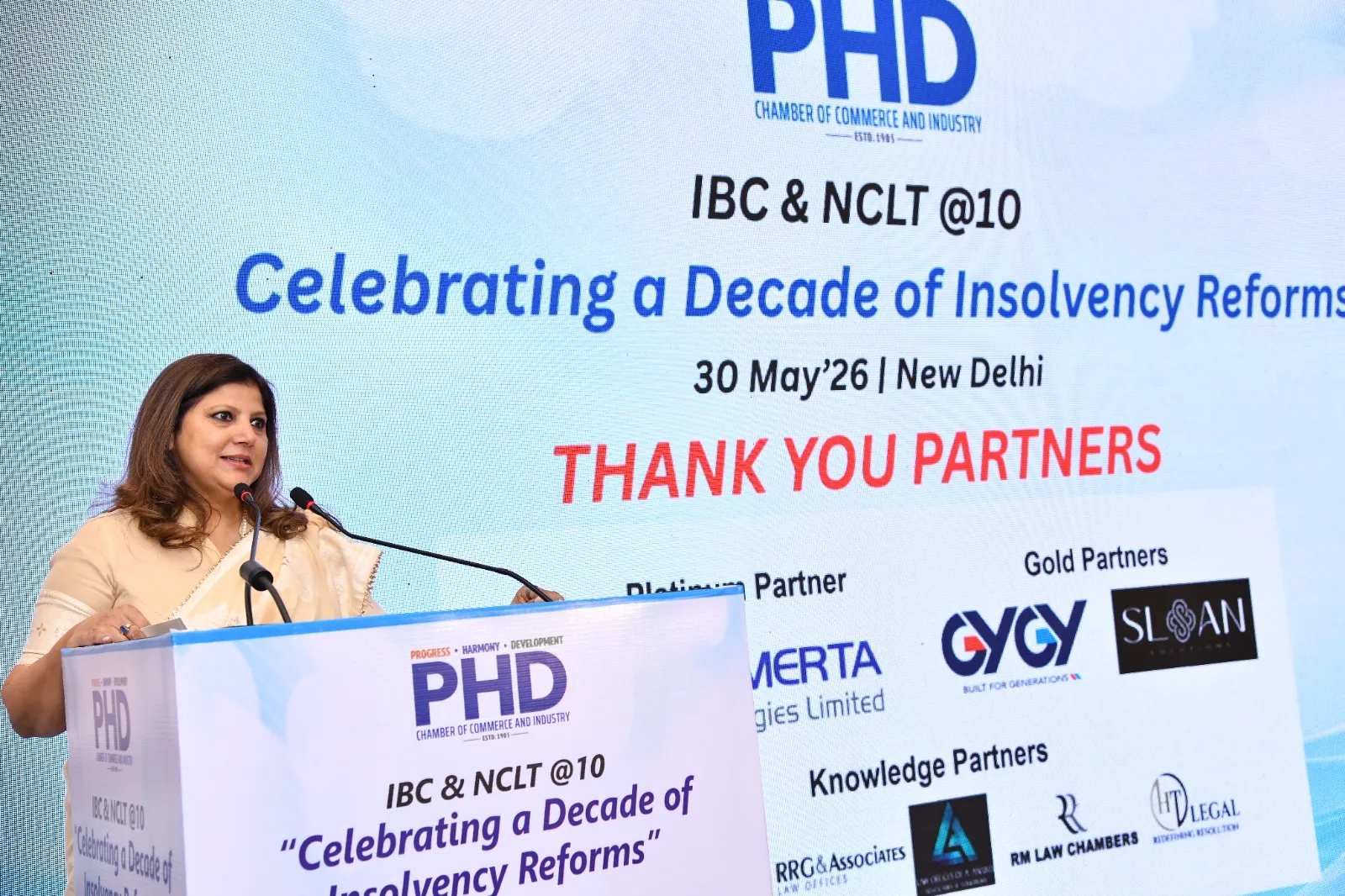 Speaker presenting at a legal event focused on insolvency reforms with a banner displaying event details and partners.