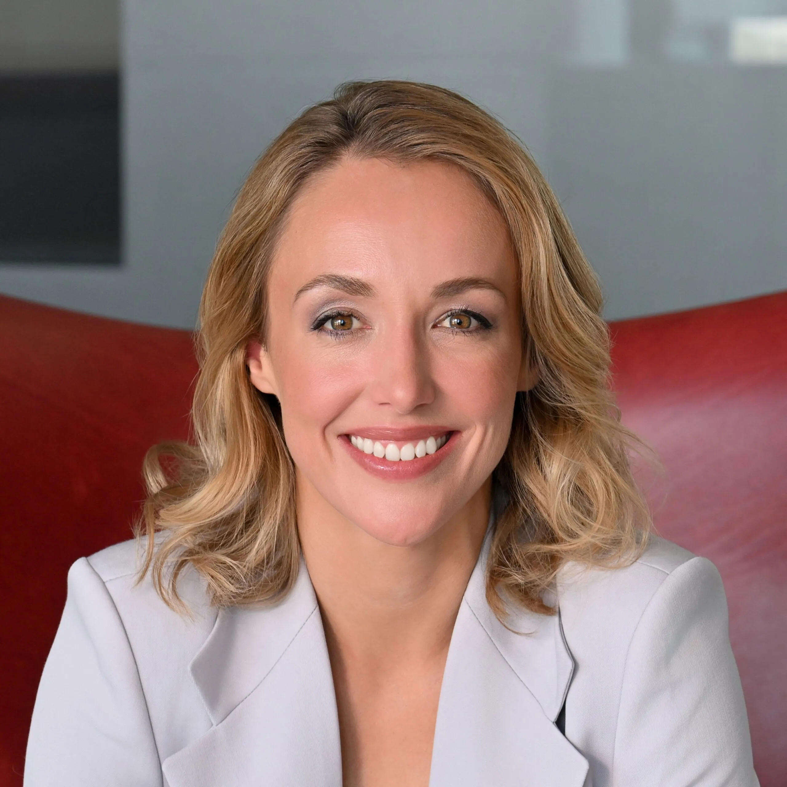 Attorney smiling, wearing a blazer, in a professional setting with a modern background.