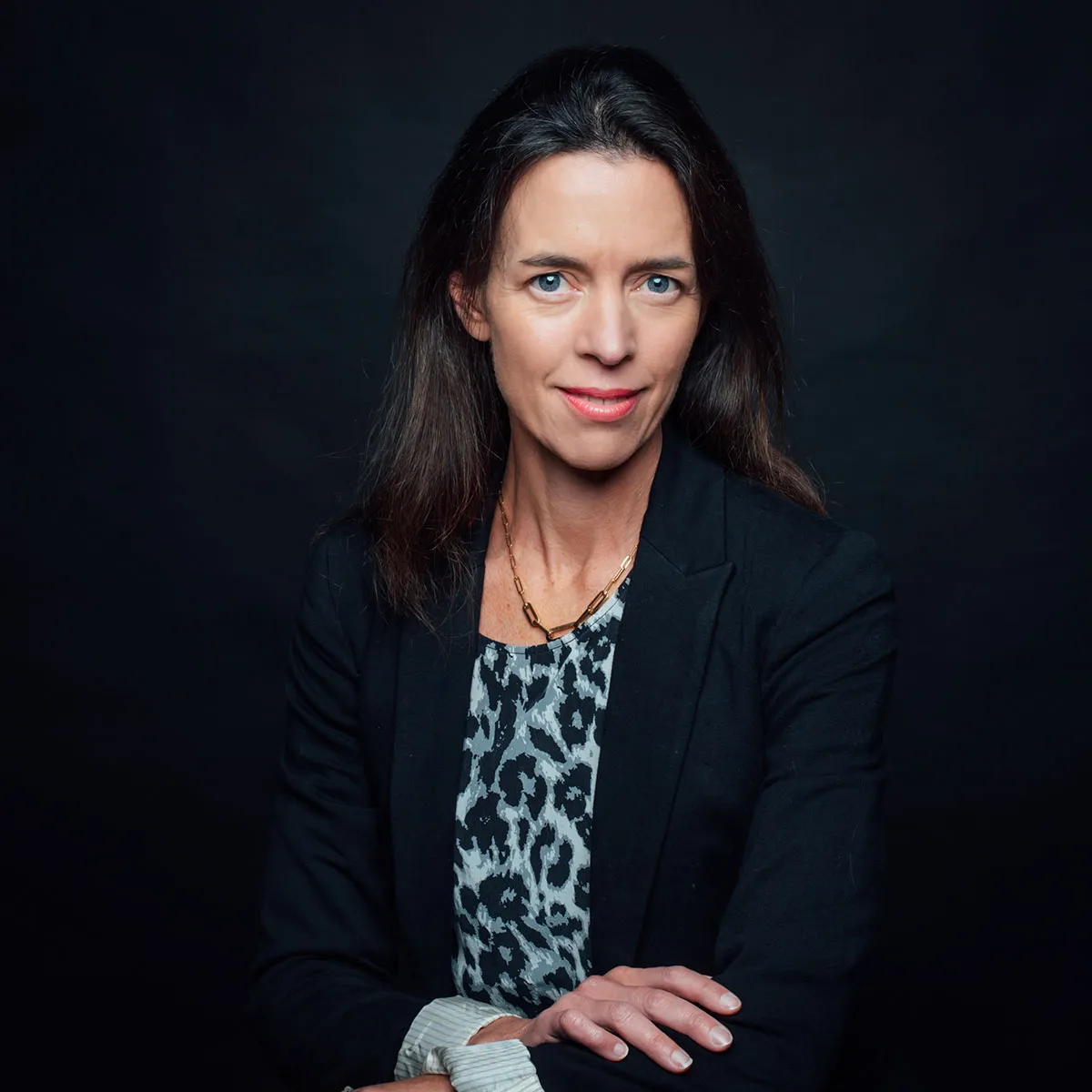 Professional woman in a black blazer and patterned top, posing confidently against a dark background.
