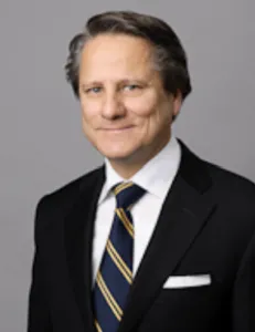 Lawyer in a suit, smiling, with a neutral background suitable for a professional profile.