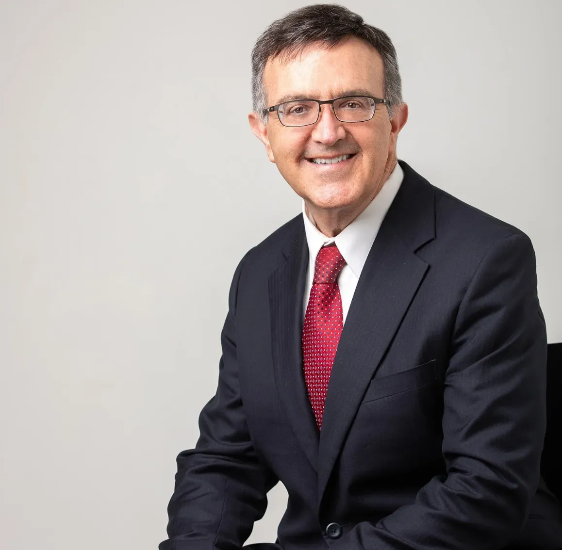 Professional lawyer sitting confidently in a suit against a neutral background.