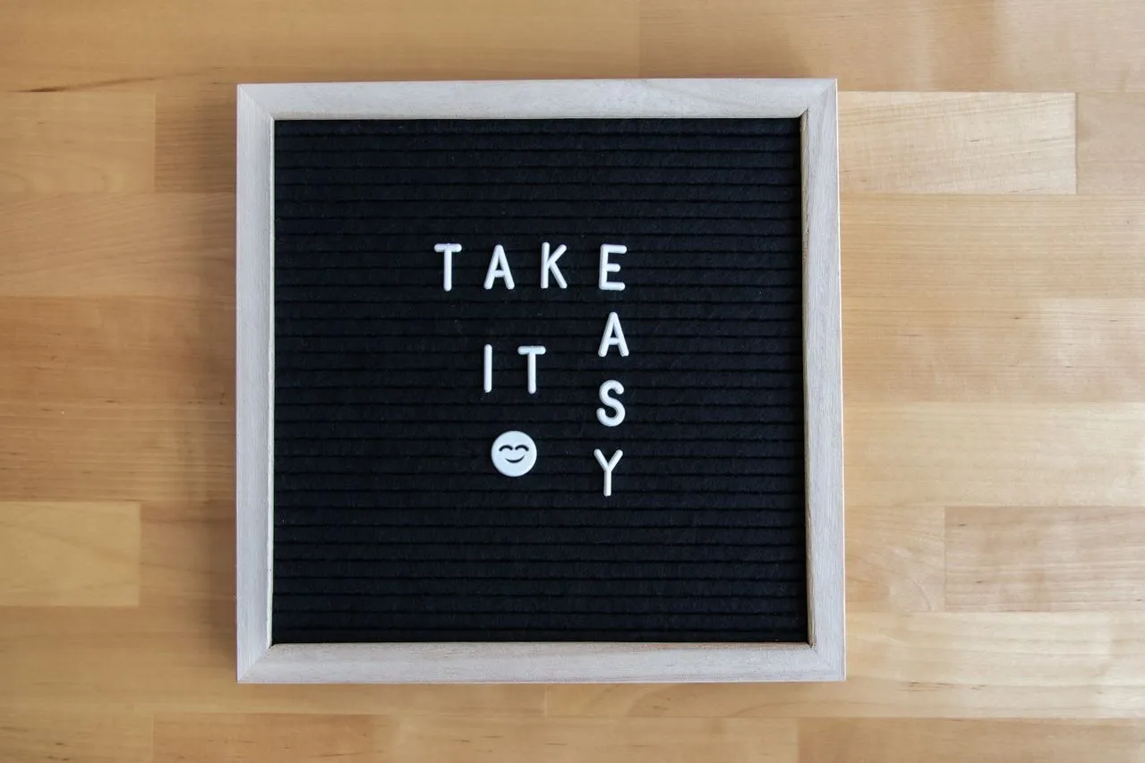 Letter board displaying the phrase "TAKE IT EASY" with a smiley face emoji against a black background.