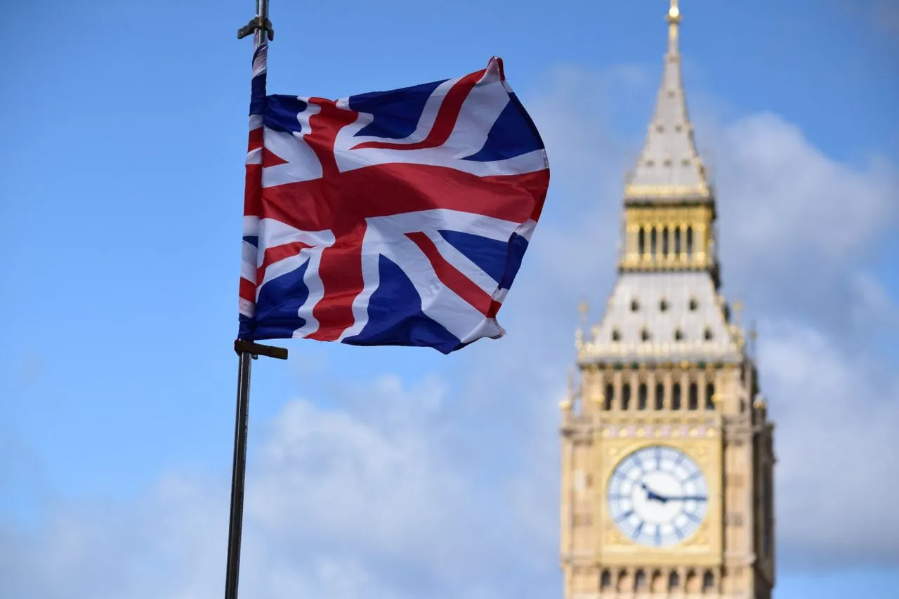 Union Jack flag waving in front of the Big Ben clock tower against a clear blue sky.