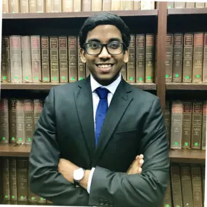 Lawyer standing confidently with arms crossed in front of a bookshelf filled with law books.