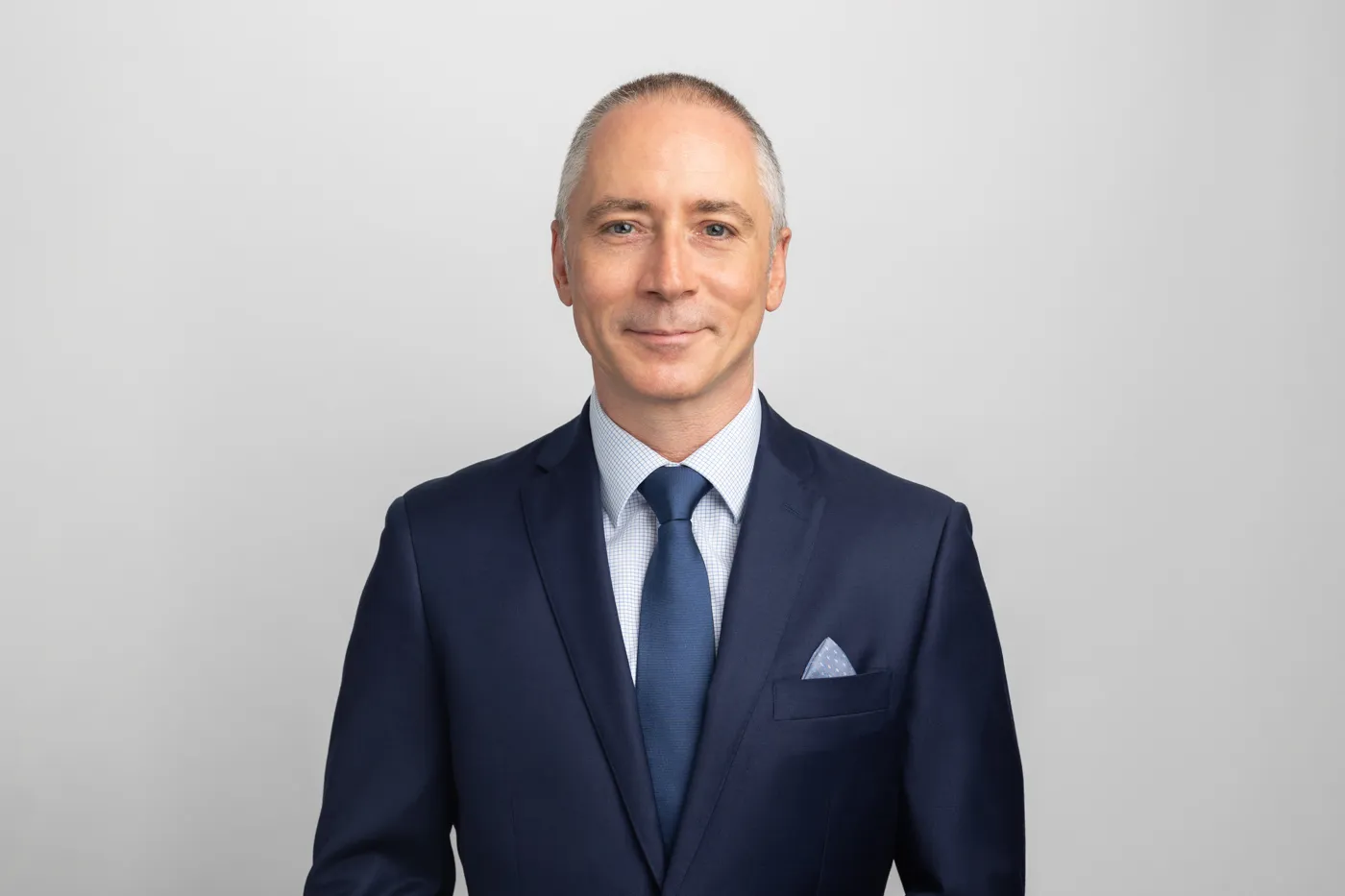Lawyer in a suit smiling against a plain background, conveying professionalism and approachability.