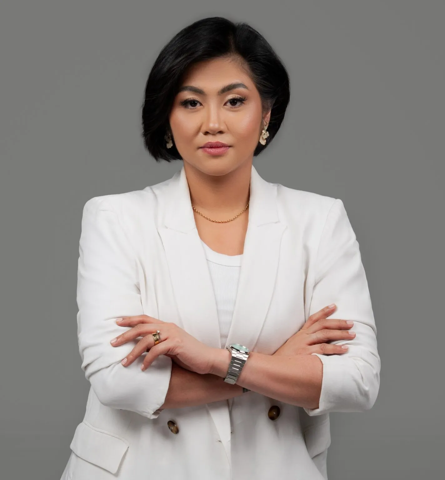 Attorney posing confidently with arms crossed, dressed in a white blazer against a neutral background.