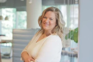 Professional woman smiling and posing in a modern office setting with soft natural light.