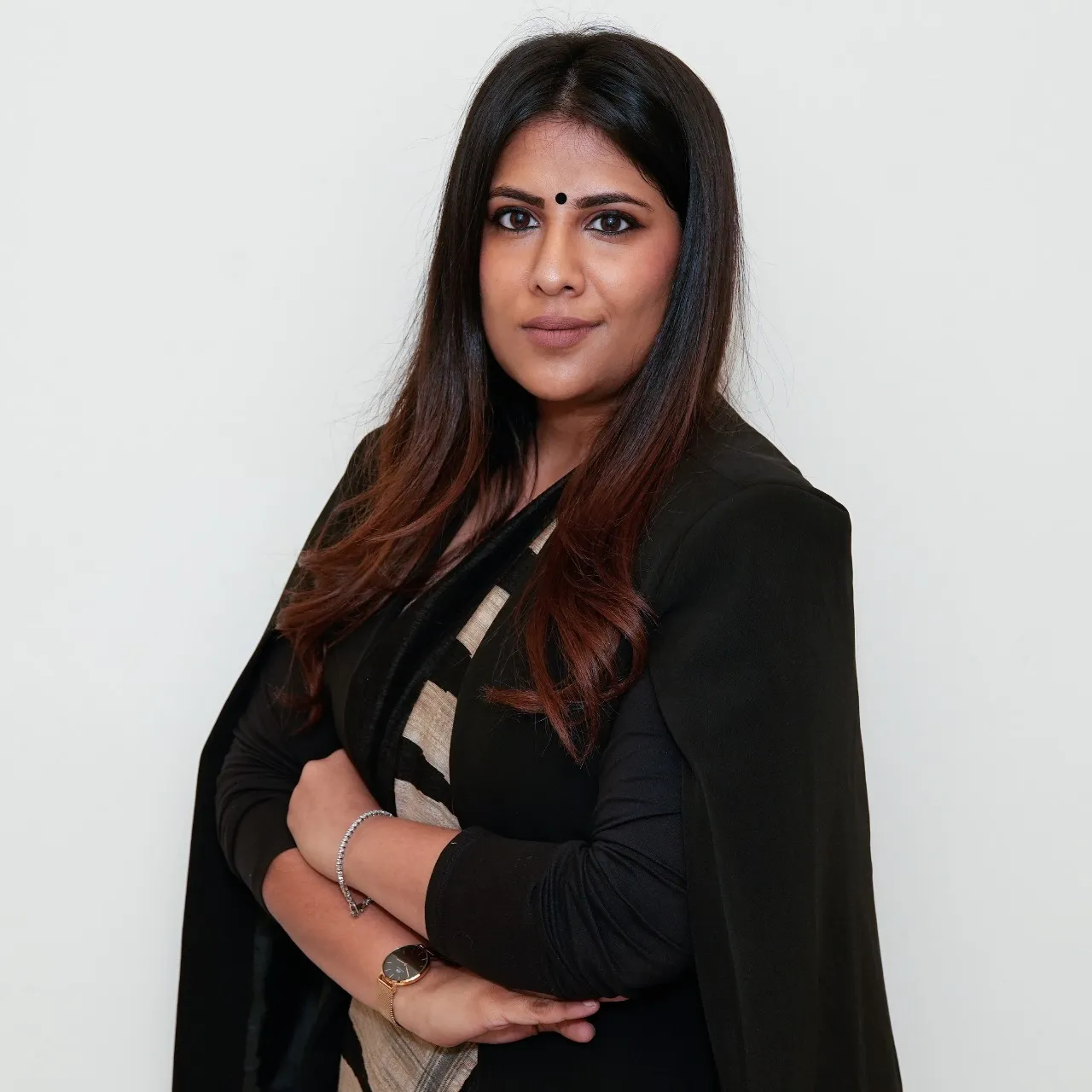 Legal professional standing with arms crossed, wearing a black blazer, in a neutral background.