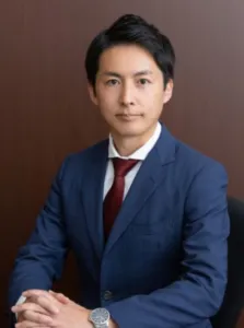 Attorney seated at a desk, wearing a suit and tie, in a professional office setting.