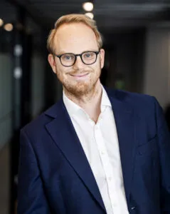 Lawyer posed in professional attire, smiling, in an office setting with modern decor.
