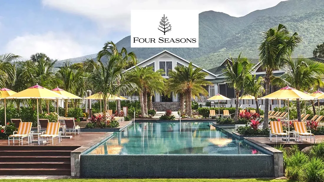 Resort pool area with lounge chairs and umbrellas, surrounded by tropical plants and mountains in the background.