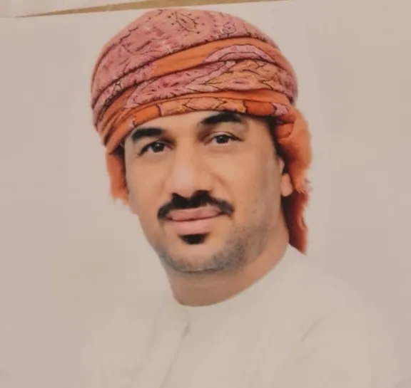 Professional wearing traditional attire with a distinctive headscarf, posing for a formal portrait.