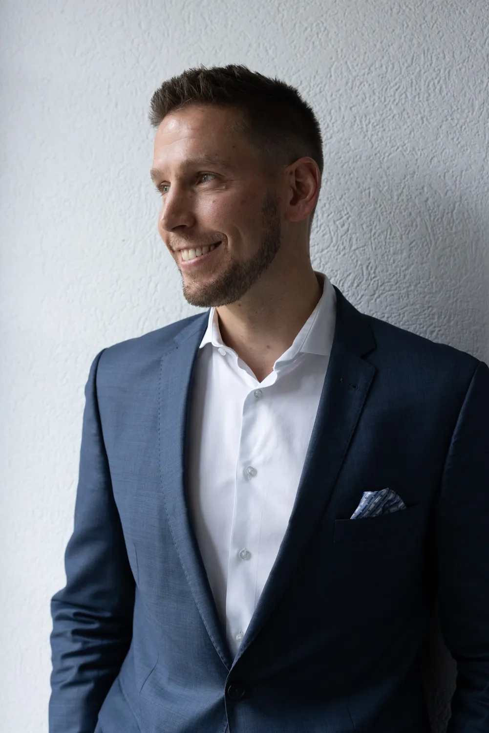 Professional man in a suit smiling against a white wall, suggesting a confident demeanor suitable for a law-related context.