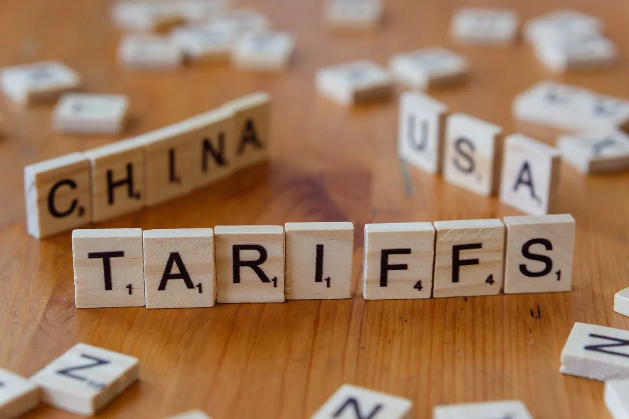 Scrabble tiles on a wooden surface spell out "CHINA" and "TARIFFS" with other scattered tiles nearby.