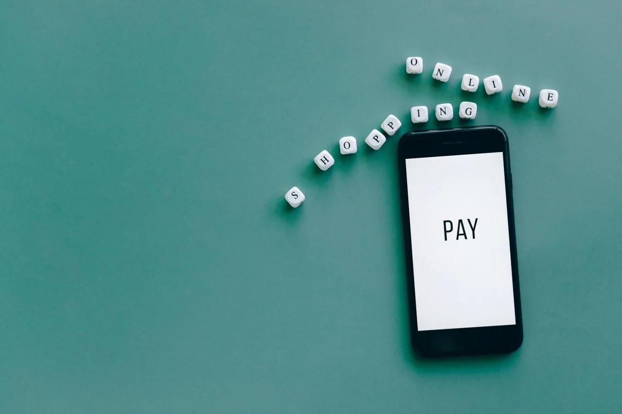 Smartphone displaying "PAY" on the screen with letter blocks arranged to spell "ONLINE SHOPPING" nearby.