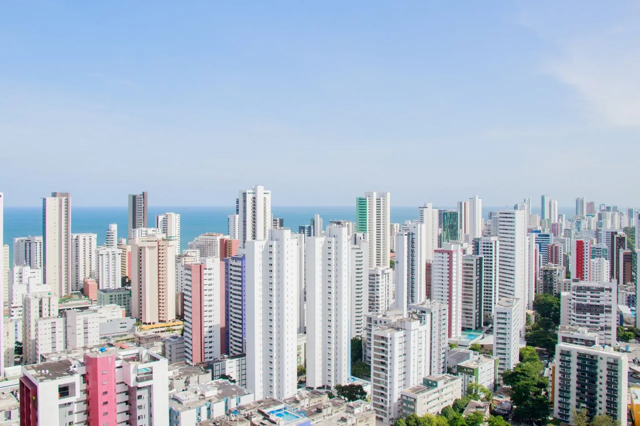 Coastal city skyline featuring high-rise buildings with ocean in the background and clear blue sky.