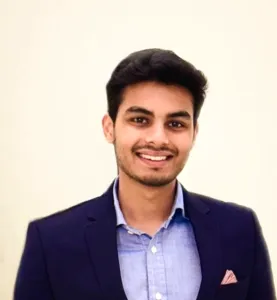 Professional smiling individual in a blazer against a neutral background.