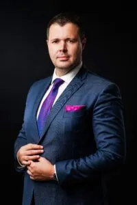 Attorney in formal attire, adjusting jacket and standing confidently against a dark background.