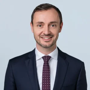 Professional lawyer smiling against a neutral background, wearing a dark suit and patterned tie.