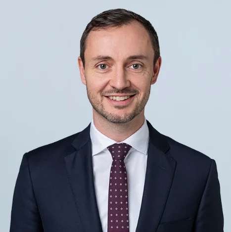 Professional lawyer smiling against a neutral background, wearing a dark suit and patterned tie.